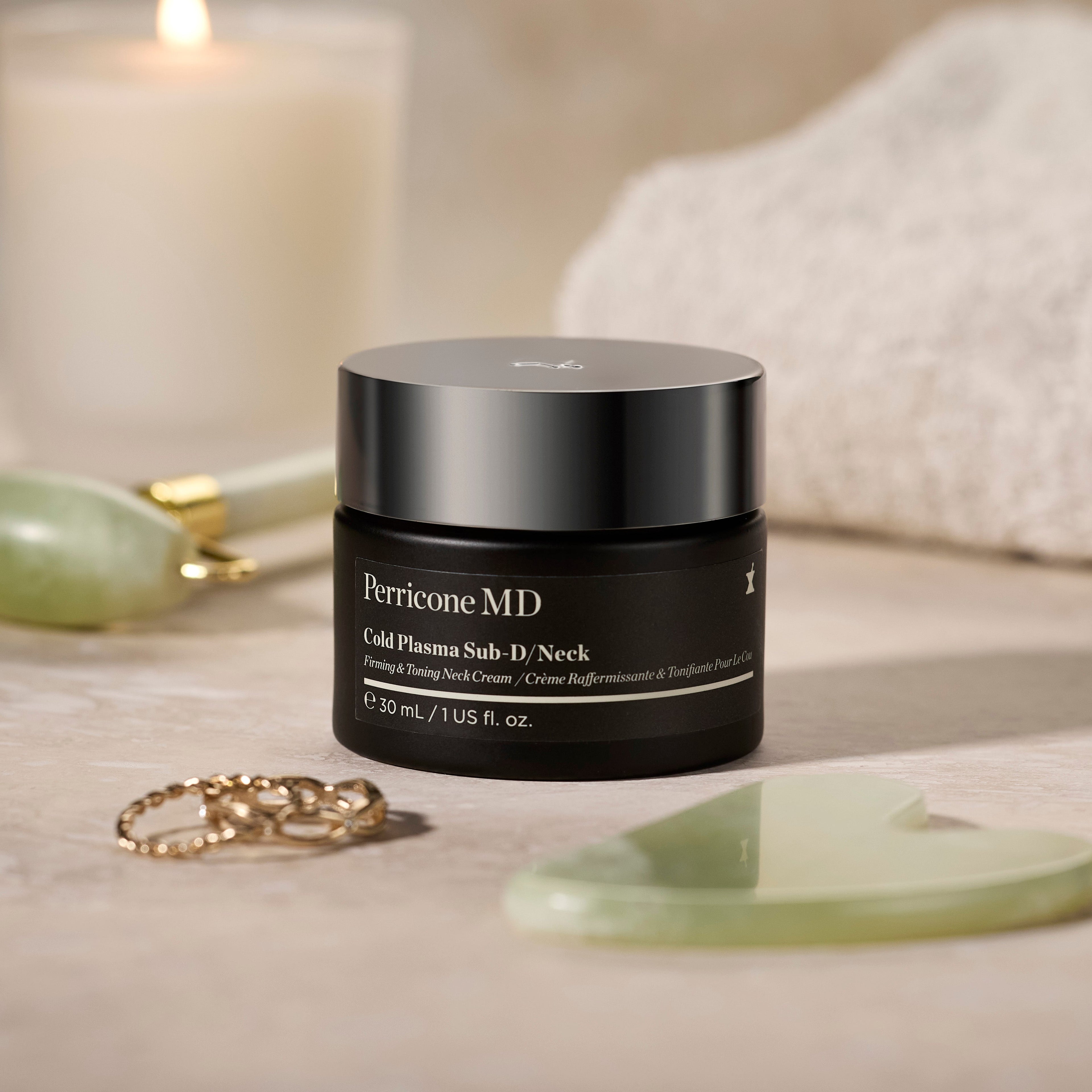 A jar of Cold Plasma Sub-D/Neck, styled on a neutral surface with a lit candle, white towel, and jade roller in the background.